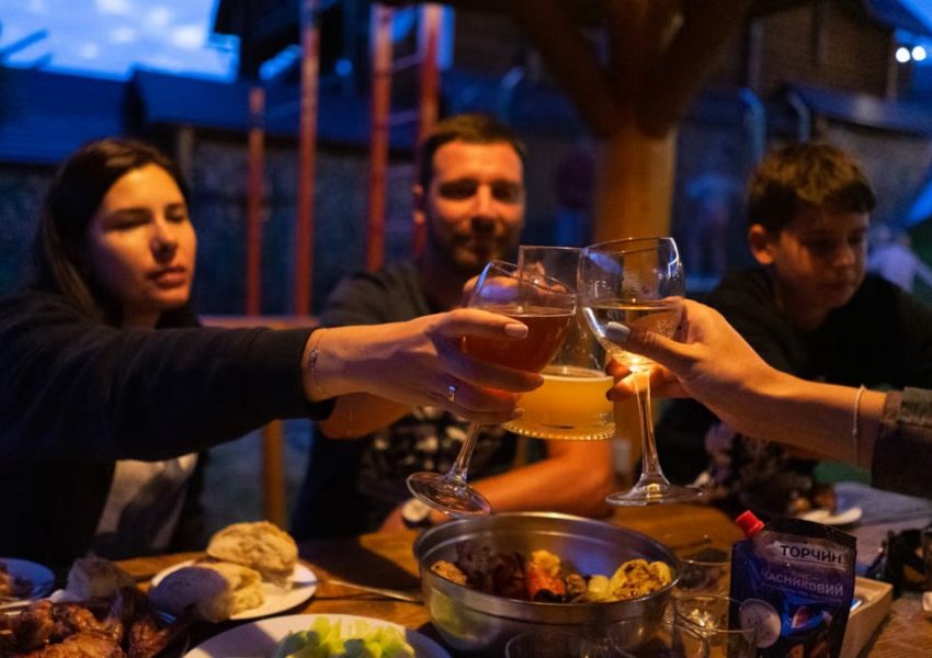 Friends clinking glasses at an outdoor dinner party, enjoying food and drinks.