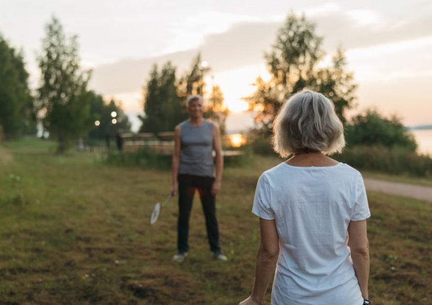 Elderly couple playing badminton outdoors at sunset, enjoying leisure time together.