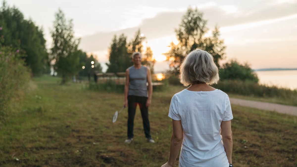 Elderly couple playing badminton outdoors at sunset, enjoying leisure time together.