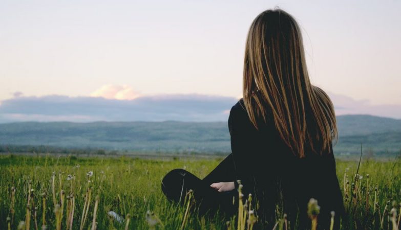 Woman enjoying peace in a lush green field with a scenic mountain view during sunset.