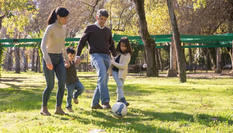 A family plays soccer together in a sunny park, enjoying quality time outdoors.